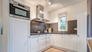 A modern kitchen with white cabinets, a stainless steel oven, and a window with a view of trees. - Villa in Domburg near North Sea Beach (Domburg)