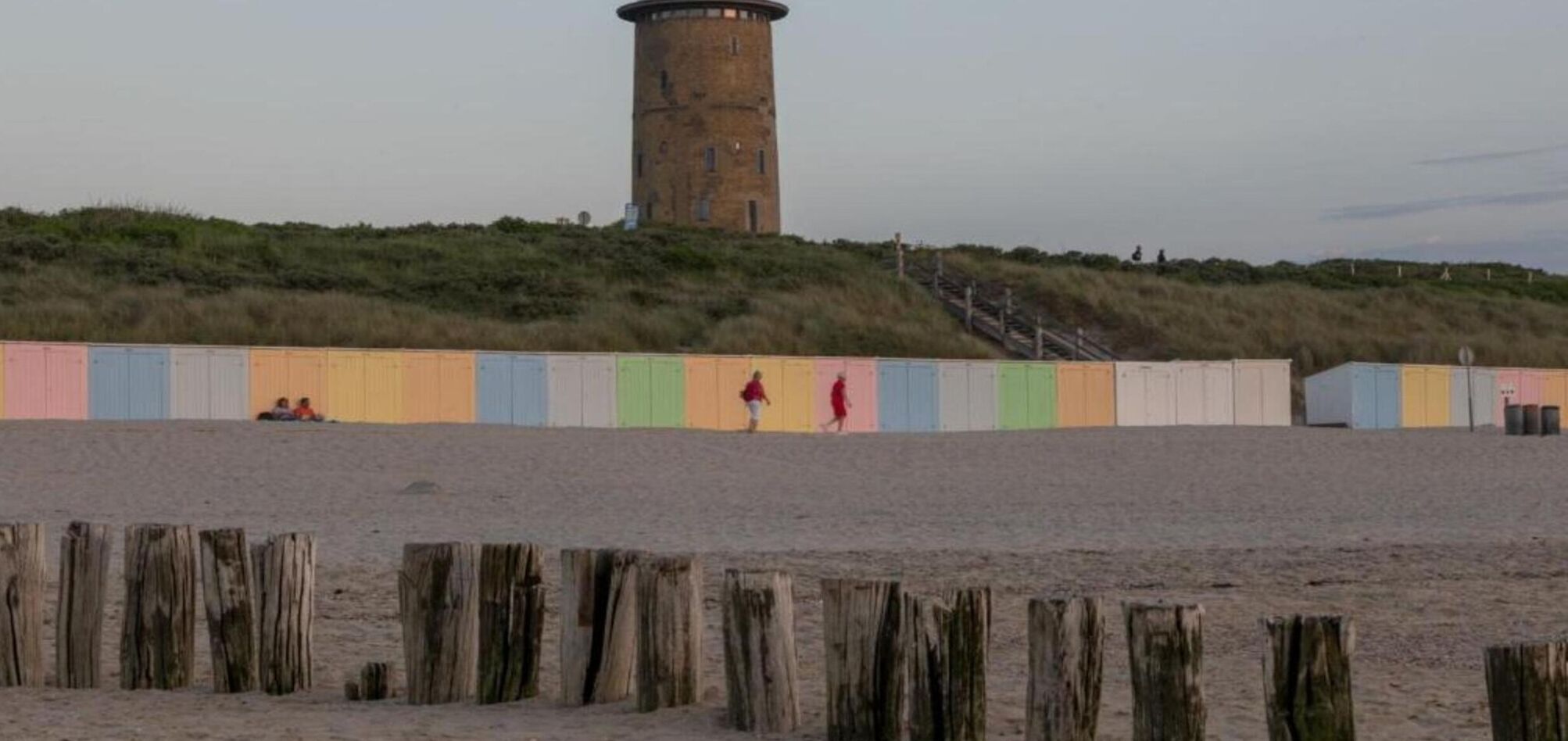 A beach with a tall tower, wooden posts, and colorful beach huts.