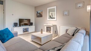 A modern living room with a sofa, coffee table, TV, and fireplace. - Villa in Domburg near North Sea Beach (Domburg)