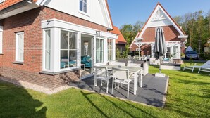 Ein zweistöckiges Haus mit Ziegelaußenwand, einem Wintergarten mit Glastüren und einer Terrasse mit Gartenmöbeln.