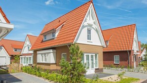 Eine Reihe moderner Häuser mit roten Ziegeldächern und weißem Zierdekor, mit einem zentralen Gartenbereich und einem kleinen Baum.