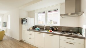 Eine moderne Küche mit weißen Schränken, einer Edelstahl-Dunstabzugshaube, einem eingebauten Backofen und einem großen Fenster, das für natürliches Licht sorgt.