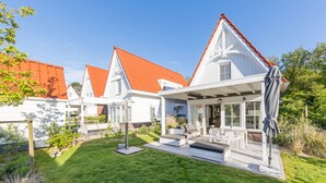 Een modern huis met een witte gevel, rood dak en een terras met tuinmeubilair.
