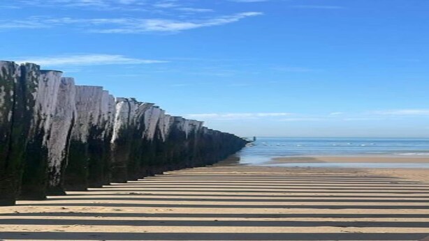 A beach with a long, straight walkway leading to the water, bordered by tall, vertical rock formations.