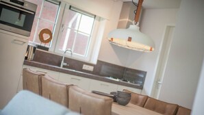A modern kitchen with a built-in oven, a dining area with a wooden table and cushioned seating, and a pendant light fixture.