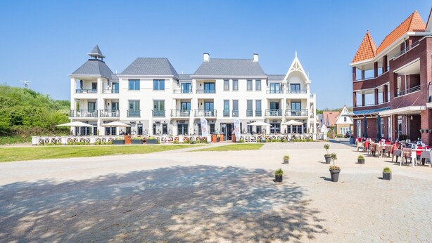 A large, multi-story building with a central courtyard, outdoor seating area, and a flag display. - Apartment near Noordzee Dishoek Beach (Koudekerke)