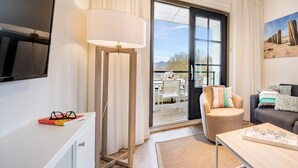 A modern living room with a flat-screen TV, a floor lamp, a sofa, a chair, and a dining area with a table and chairs. - Apartment near Noordzee Dishoek Beach (Koudekerke)