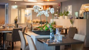 A restaurant interior with tables set for dining, a central floral arrangement, and ambient lighting. - Apartment near Noordzee Dishoek Beach (Koudekerke)