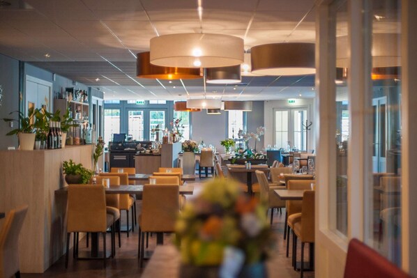 A modern restaurant with a long counter, multiple tables, and hanging pendant lights.