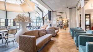 A spacious lobby with a wooden floor, a large seating area with sofas and armchairs, and a central decorative plant.
