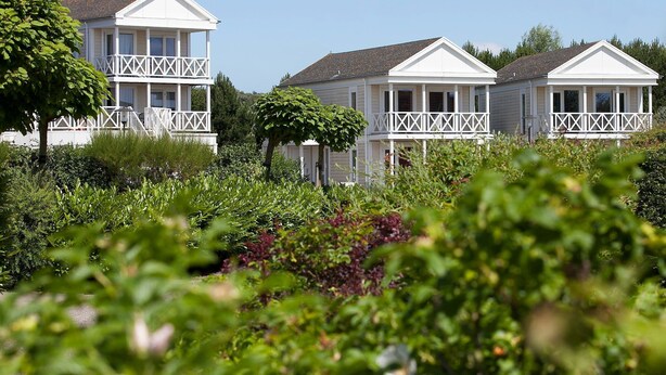 A row of white, two-story cottages with balconies, surrounded by lush greenery.