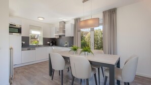 Een moderne keuken met witte kasten, een ingebouwde oven en een eethoek met een tafel en stoelen.