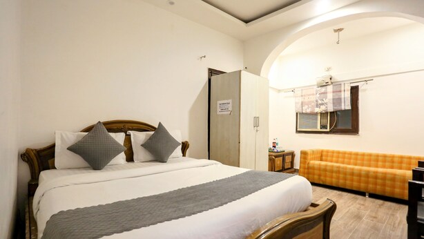 A bedroom with a bed, a sofa, a wardrobe, and a mirror. - Hotel Shilo inn  (New Delhi)