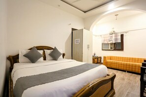 A bedroom with a bed, a sofa, a wardrobe, and a mirror. - Hotel Shilo inn  (New Delhi)