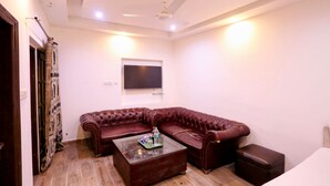 A living room with a brown leather sofa, a glass coffee table, and a ceiling fan. - Hotel Shilo inn  (New Delhi)