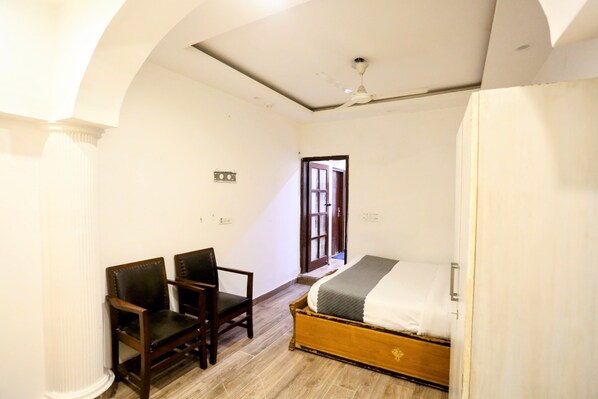 A room with a bed, two chairs, a ceiling fan, and a door leading outside.