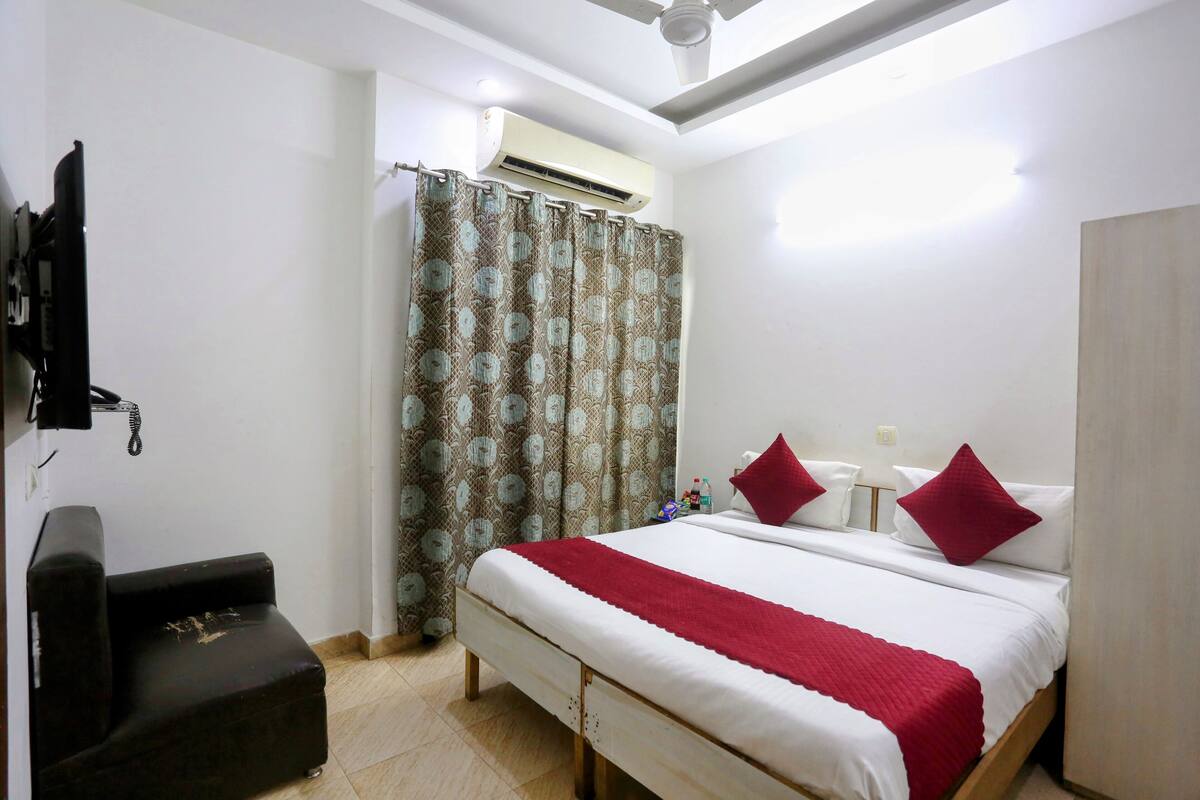 A hotel room with a bed, a chair, an air conditioner, and a curtain.