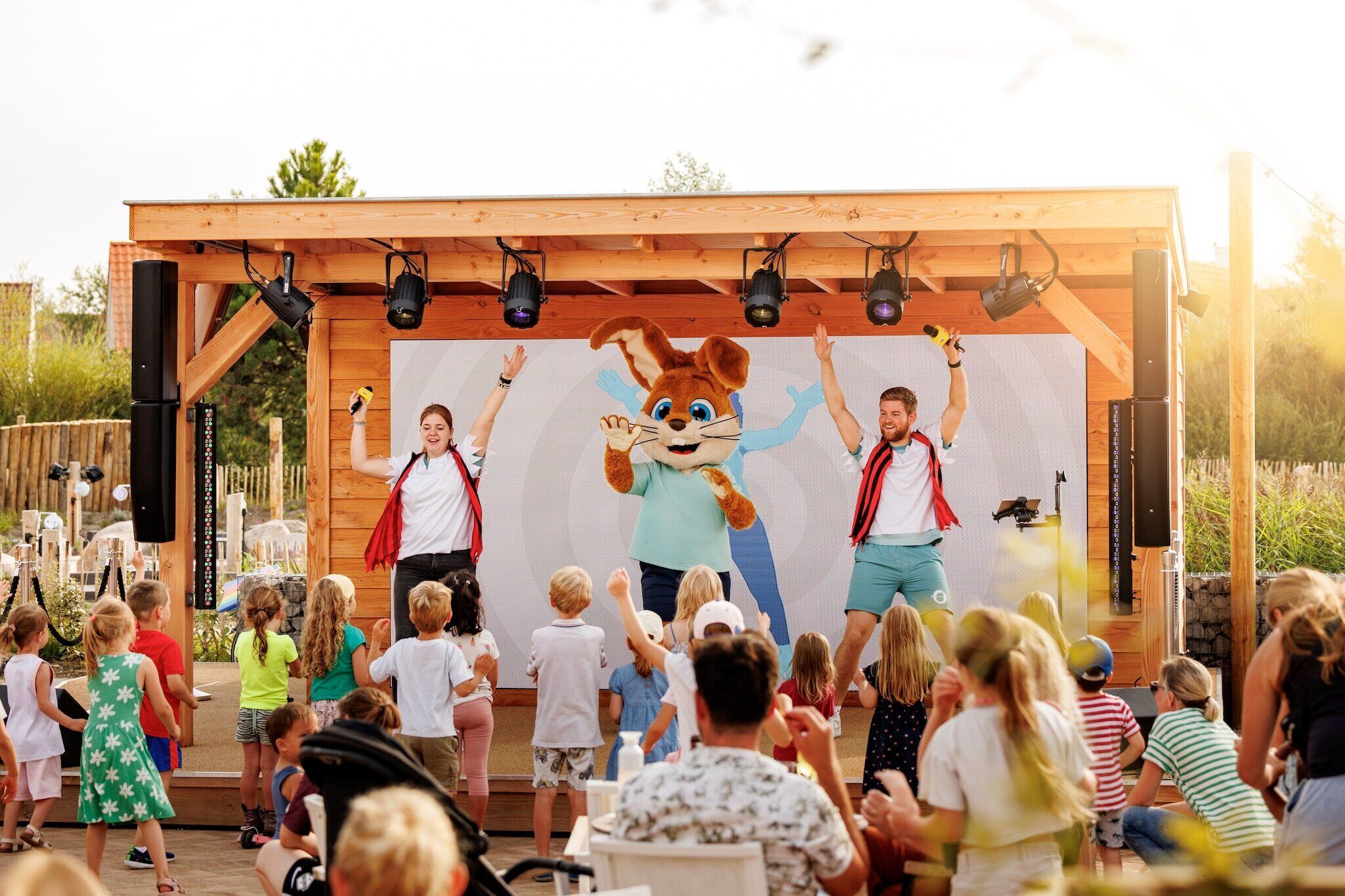 A stage with a large mascot and two performers, surrounded by an audience.
