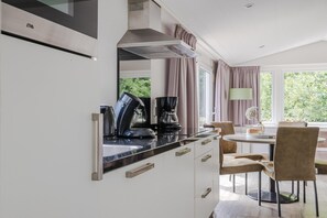 A modern kitchen with a built-in stove, a coffee maker, and a dining area with a table and chairs. - Chalet in Arcen with Private Terrace (Arcen)