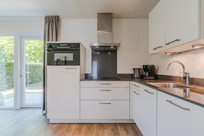 A modern kitchen with a built-in oven, a coffee maker, and a stainless steel sink. - Nature-Set Villa with Microwave Oven (Arcen)