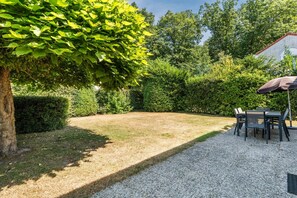 A garden with a gravel path, a table with chairs, and a tree providing shade. - Nature-Set Villa with Microwave Oven (Arcen)