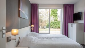 Hotellihuone, jossa on sänky, televisio, kaappi ja ikkuna, jossa on violetit verhot.