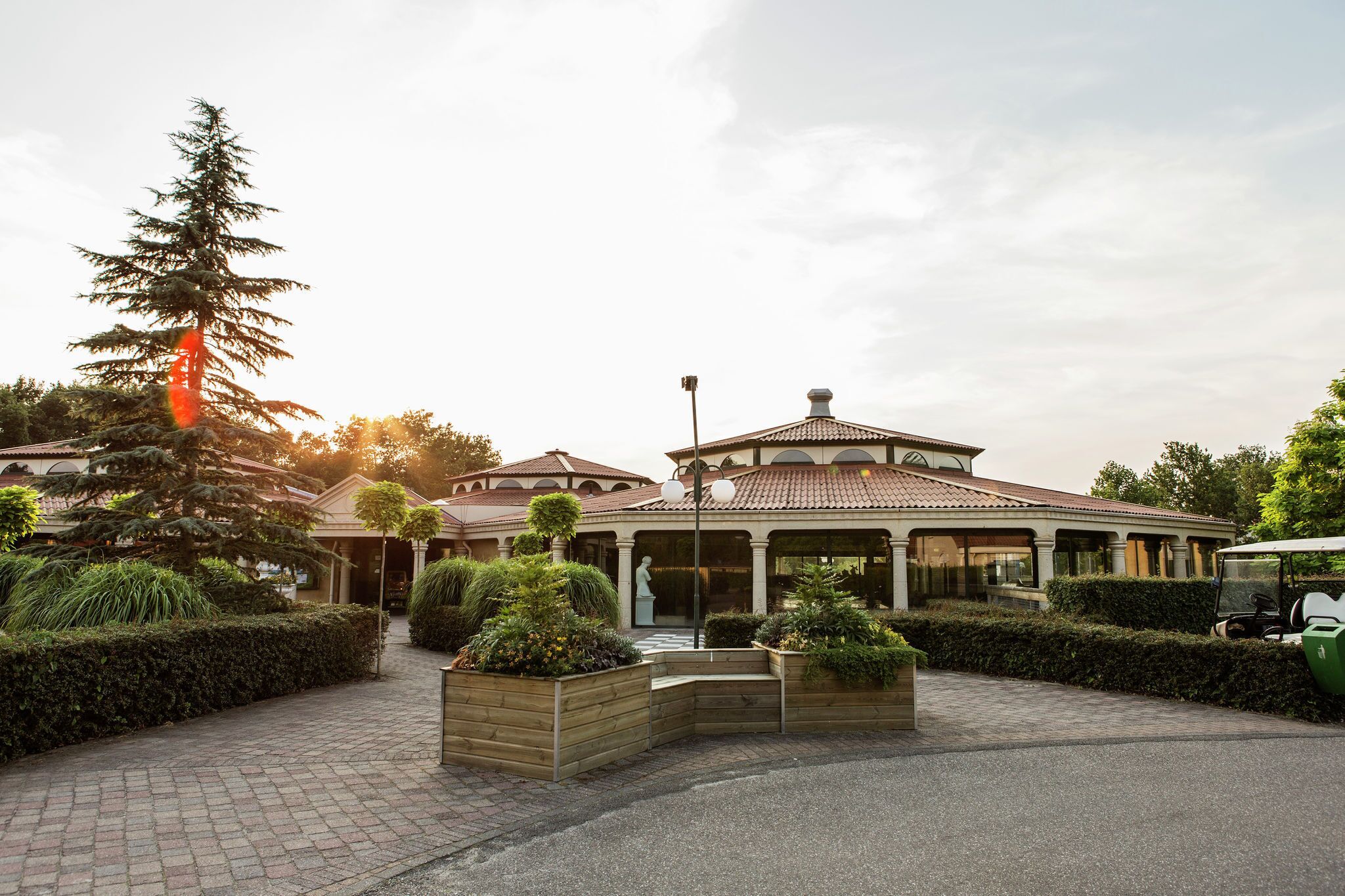 A building with a tiled roof and a central dome, surrounded by well-maintained hedges and planters.