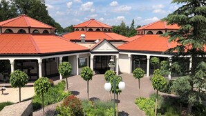 A courtyard with a central fountain, surrounded by trees and lamp posts, leading to a building with multiple red-roofed structures. - Modern Bungalow with Washer (Arcen)