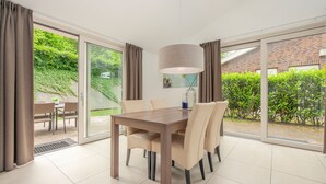 A dining area with a table and chairs, large windows, and a view of greenery outside. - Modern Bungalow with Washer (Arcen)