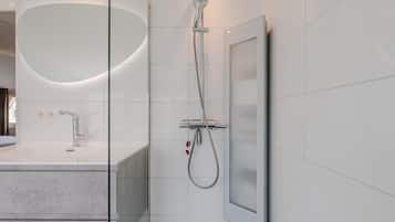 A modern bathroom with a glass shower enclosure, a large mirror, and a marble countertop.