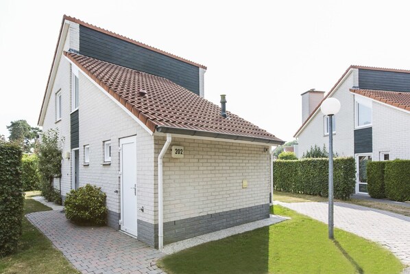 A modern two-story residential building with a tiled roof, numbered 202, featuring a brick facade, a small front yard, and a paved driveway.