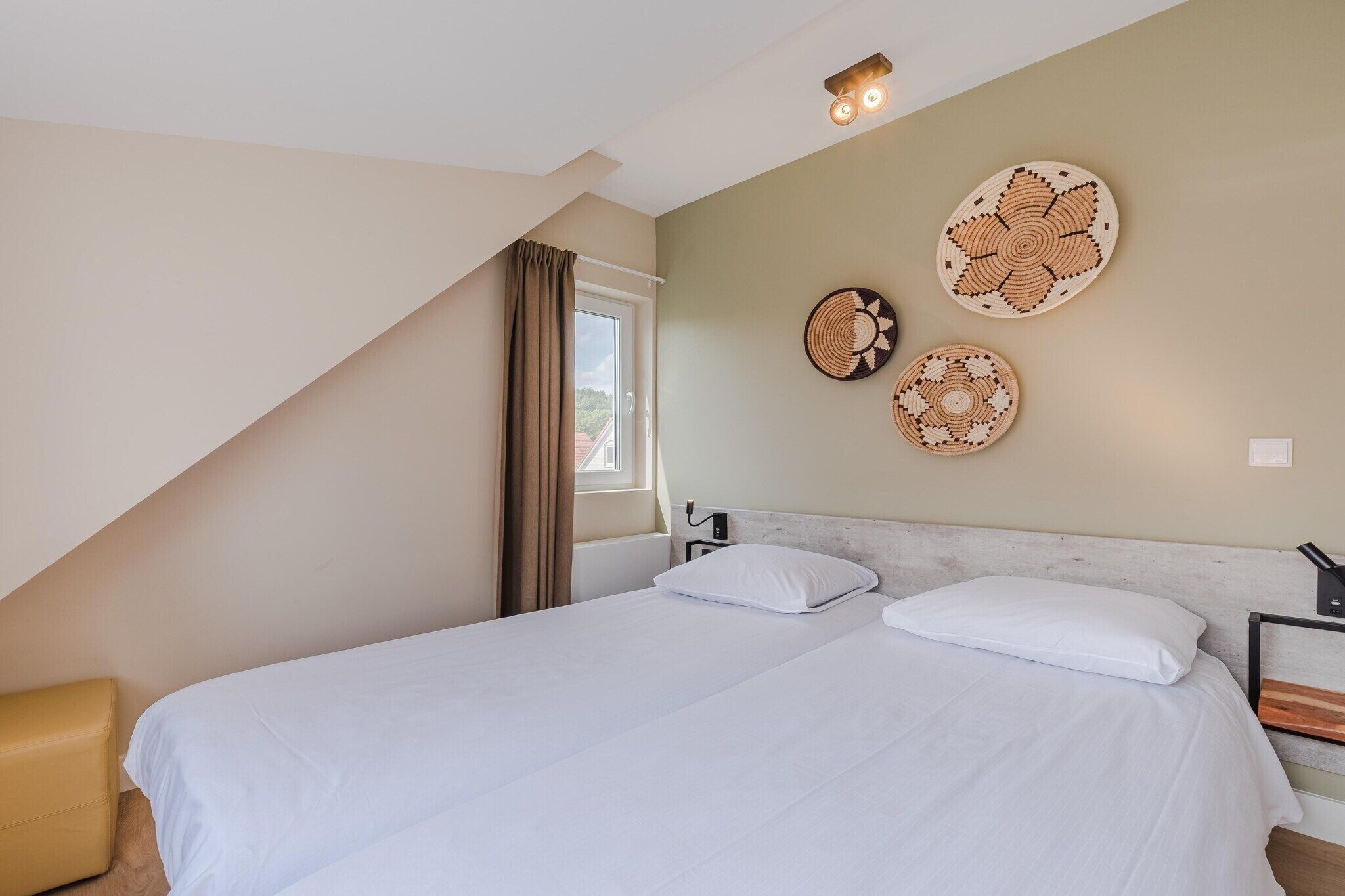 A bedroom with a bed, two pillows, a headboard, a window with curtains, and wall decor.