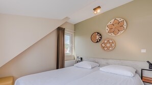 Quarto com cama, duas almofadas, cabeceira, janela com cortinas e decoração na parede.