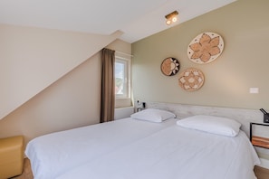 A bedroom with a bed, two pillows, a headboard, a window with curtains, and wall decor.