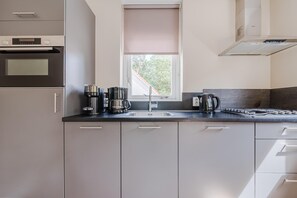 A modern kitchen with a built-in oven, a coffee maker, a kettle, and a sink.