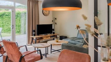 Een moderne woonkamer met een televisie, twee banken, een salontafel en een groot raam met gordijnen.