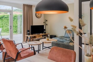 A modern living room with a television, two sofas, a coffee table, and a large window with curtains. - High-End Villa Nestled in Greenery (Arcen)