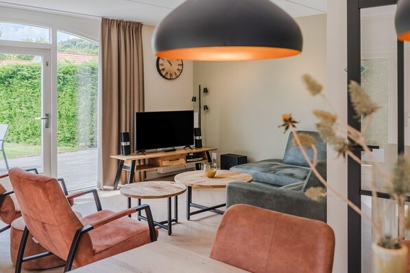 A modern living room with a television, two sofas, a coffee table, and a large window with curtains.