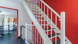 Una escalera con barandillas blancas y paredes rojas, que lleva a una habitación con una cama y un ventanal.