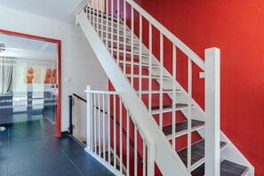 A staircase with white railings and red walls, leading to a room with a bed and a window. - Group Getaway in Arcen (Arcen)