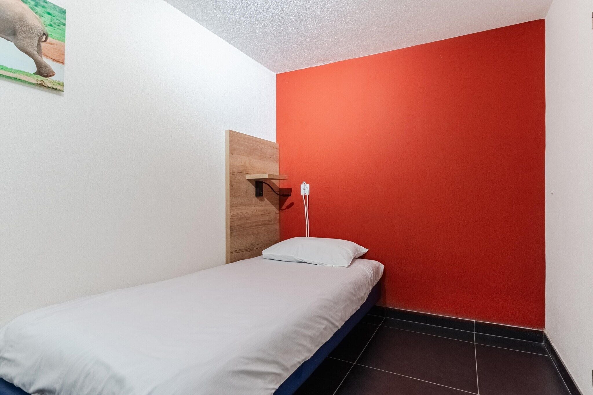 A small, single-bed room with a red accent wall, a wooden headboard, and a white pillow.