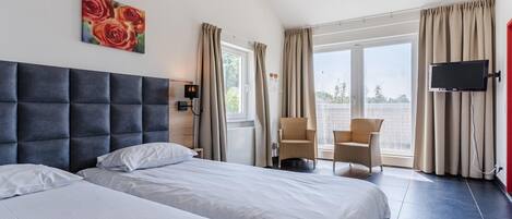 Ein Hotelzimmer mit zwei Betten, einem Fernseher, einem Fenster mit Vorhängen und einem Bild an der Wand.