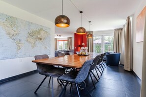 A modern dining area with a large wooden table, black chairs, and pendant lighting. - Group Getaway in Arcen (Arcen)