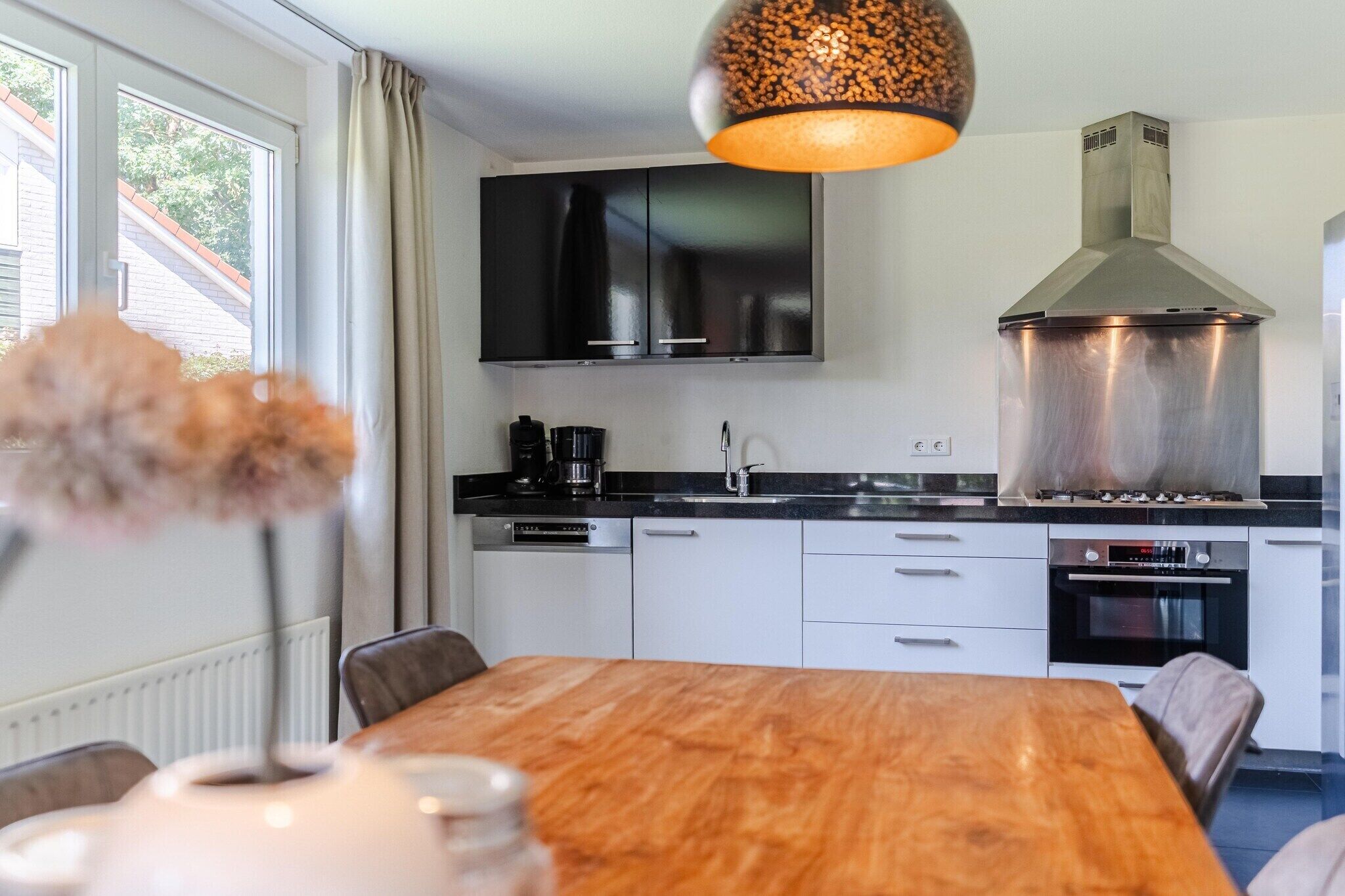 Een moderne keuken met een houten eettafel, zwarte kasten en roestvrijstalen apparatuur.