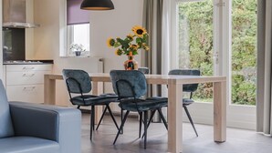 Moderni keittiö, jossa on ruokailutila, suuri ikkuna, josta avautuu näkymä vehreään maisemaan, sekä pöydällä oleva maljakko, jossa on auringonkukkia.