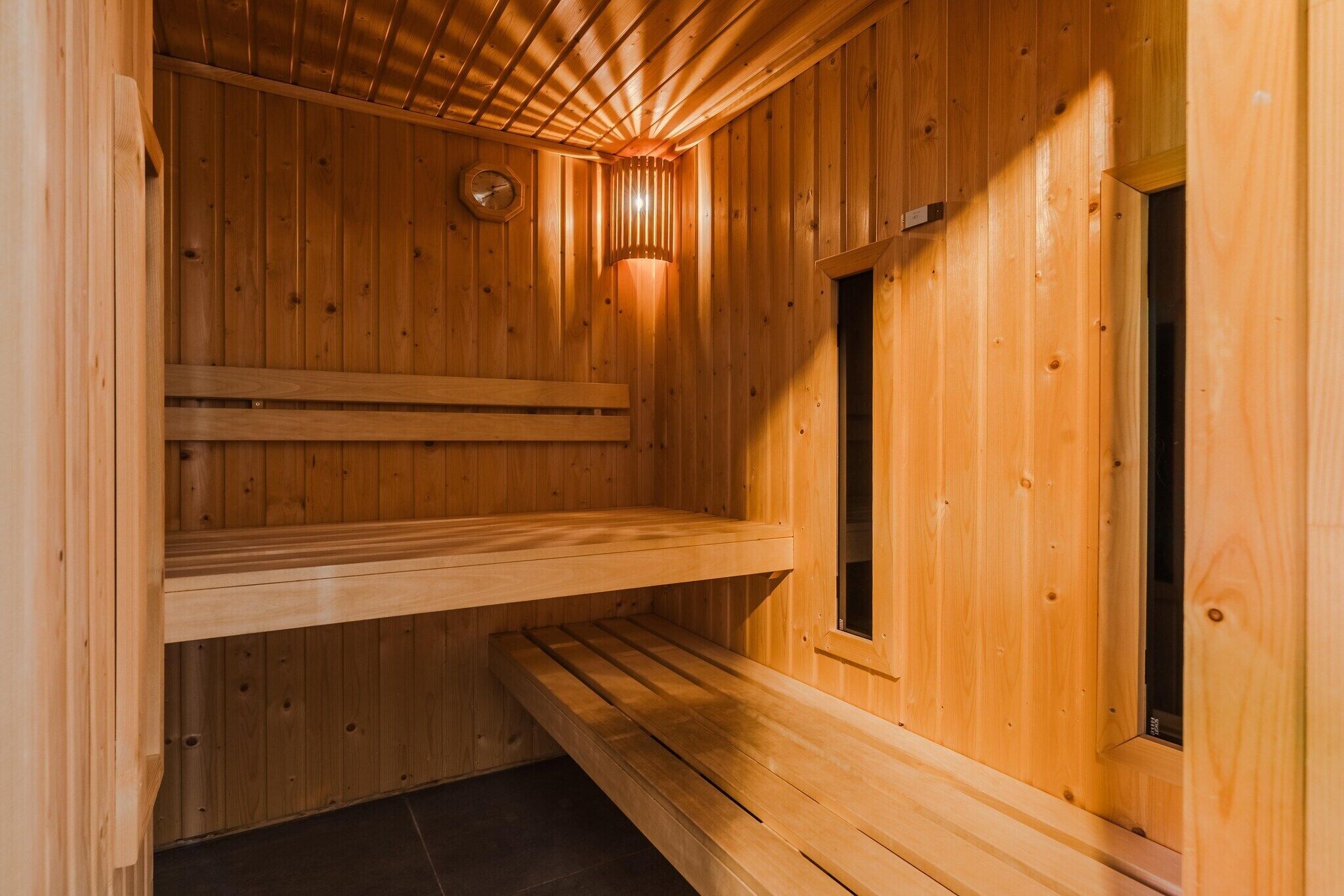 A wooden sauna with a sloped ceiling, a bench, and a wall-mounted clock.