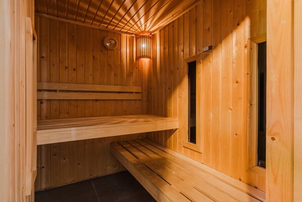 A wooden sauna with a sloped ceiling, a bench, and a wall-mounted clock.