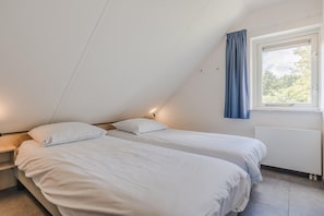 A bedroom with two beds, a window with curtains, and a radiator.