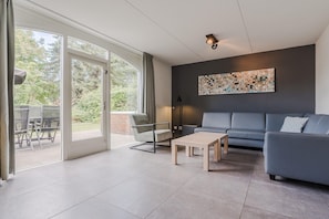 A modern living room with a grey sofa, a wooden coffee table, and a dining area with chairs and a table.