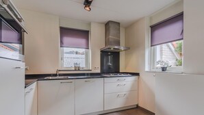 Keittiössä on valkoiset kaapit, musta työtaso, ruostumattomasta teräksestä valmistettu liesituuletin ja ikkuna, jossa on violetti sälekaihdin.